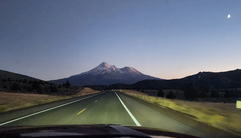 Moonlit mountain road climbing toward Mount Shasta with roadside markers guiding each curve, representing the vision to remain focused on long-term business goals while navigating the road ahead.
