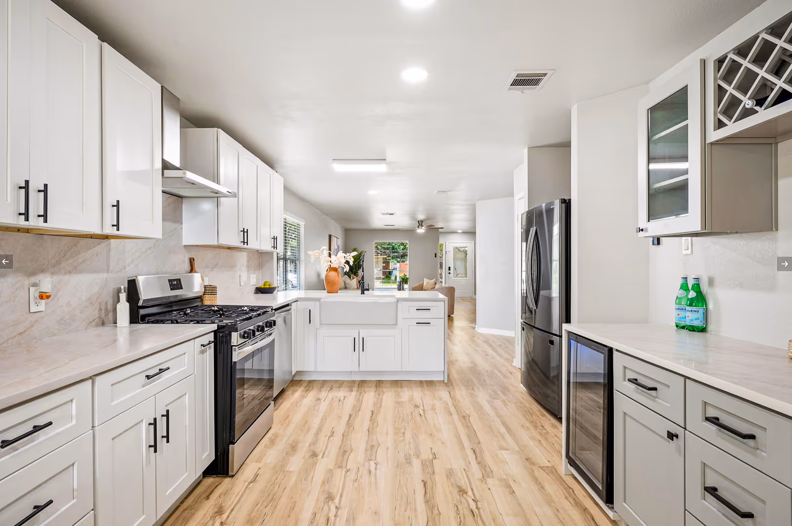 Spacious modern kitchen with white cabinets, stainless steel appliances, light wood floor, and a farmhouse sink.