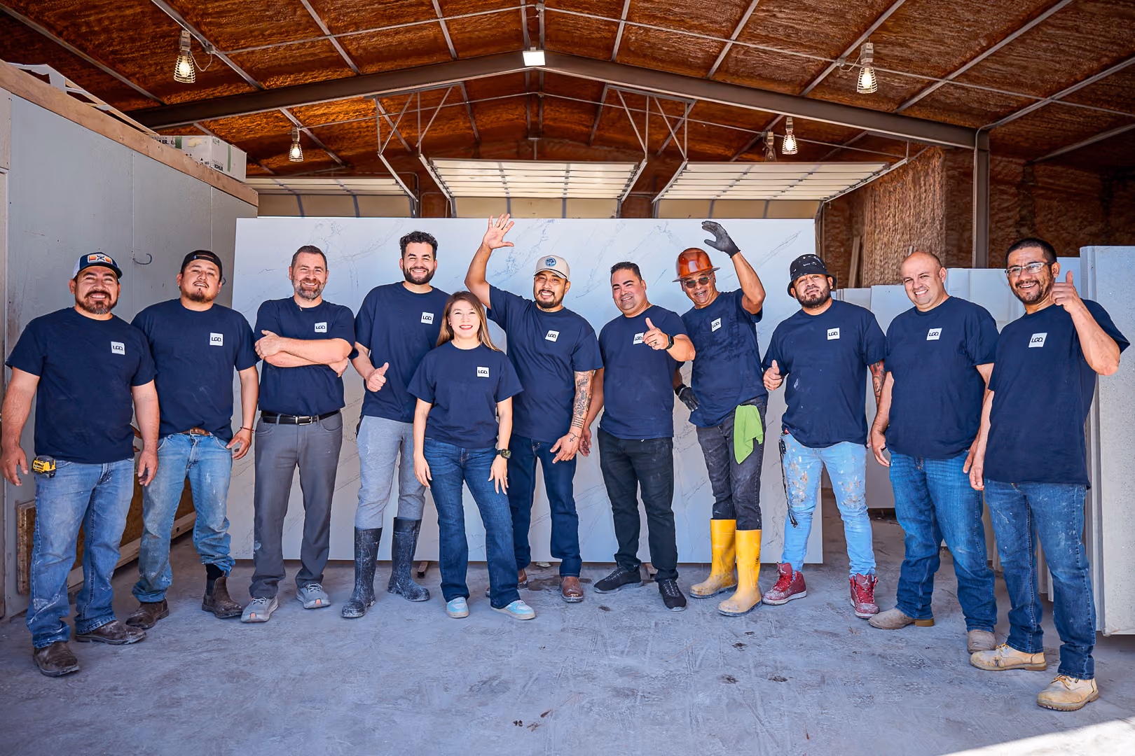 Eleven people wearing navy blue shirts pose smiling inside an industrial building.