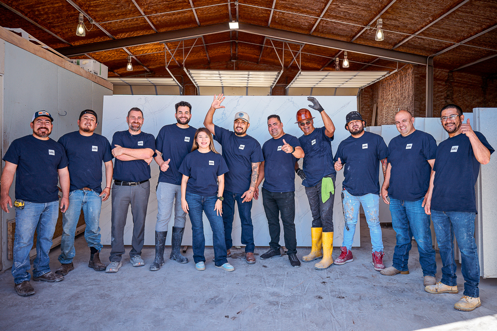 Eleven people wearing navy blue shirts pose smiling inside an industrial building.