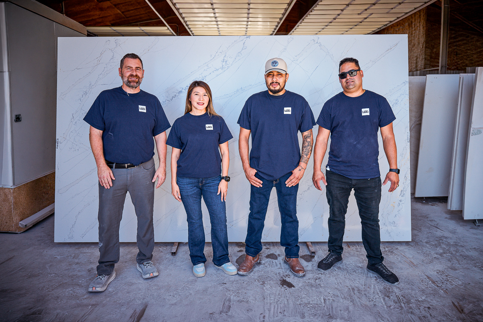 Four people standing indoors wearing navy LGD t-shirts in front of a large marble slab.