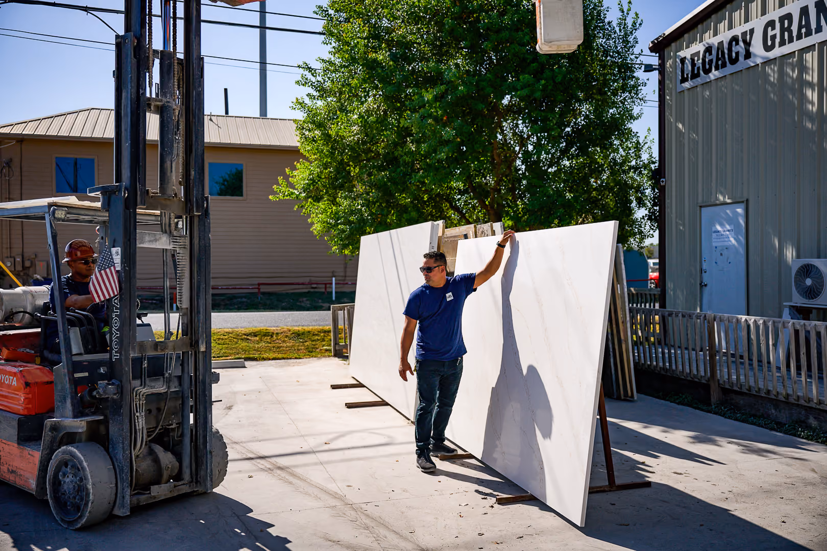 Worker inspecting large white stone slabs outside near a building and forklift with an American flag.
