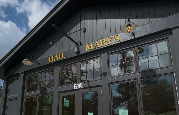 Exterior of a dark gray building with large glass windows and a sign reading HAIL MARY'S above the entrance.