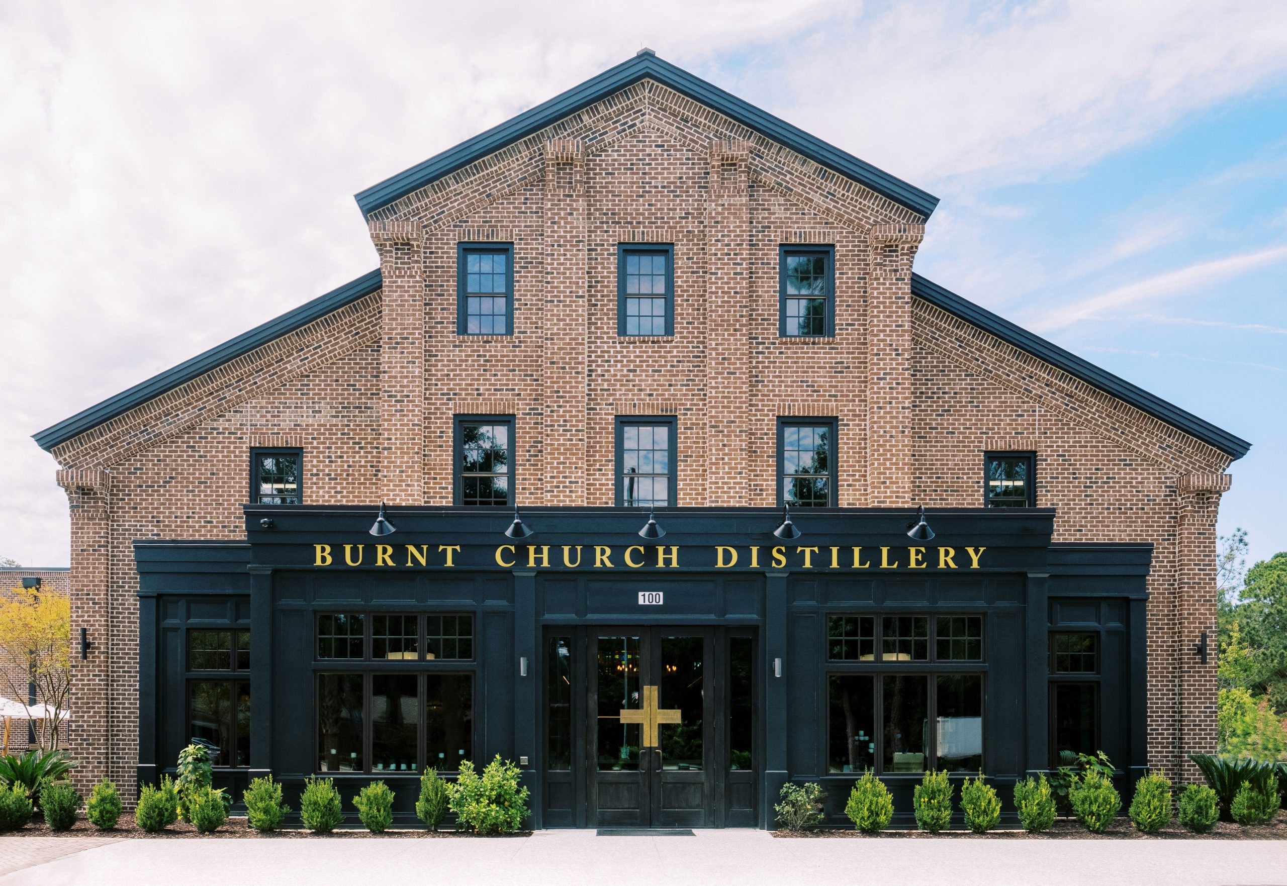 Front view of Burnt Church Distillery, a brick building with black framed windows and gold lettering above the entrance.