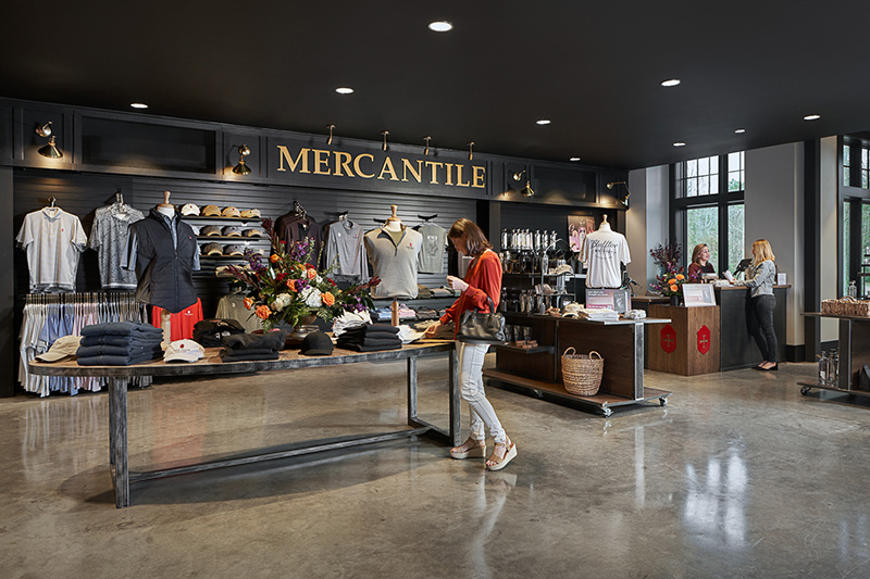 Modern retail store interior with clothing, accessories, and a woman browsing items under a Mercantile sign.