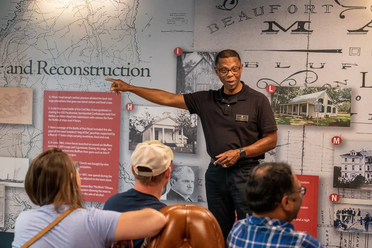 Tour guide pointing to a historical exhibit while speaking to an attentive audience.