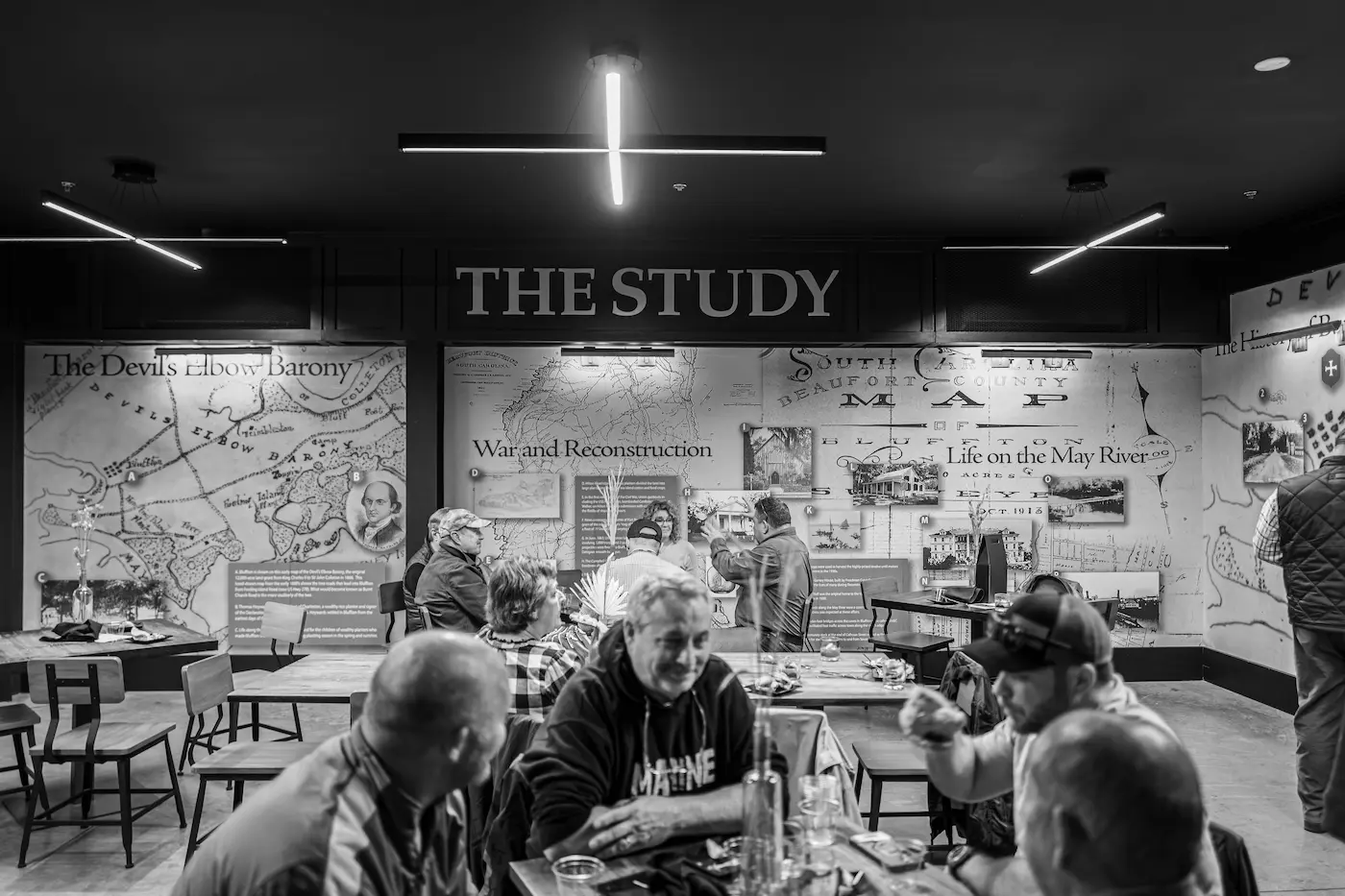 People sitting and conversing in a room with historical maps and text on the walls under a sign reading 'THE STUDY'.