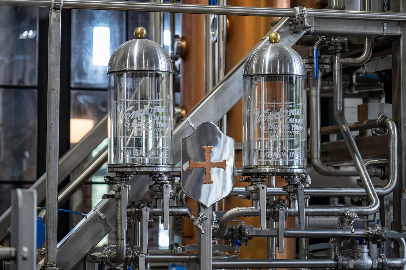 Two glass alcohol flow indicators labeled High Wine and Low Wine on stainless steel industrial distillation equipment.