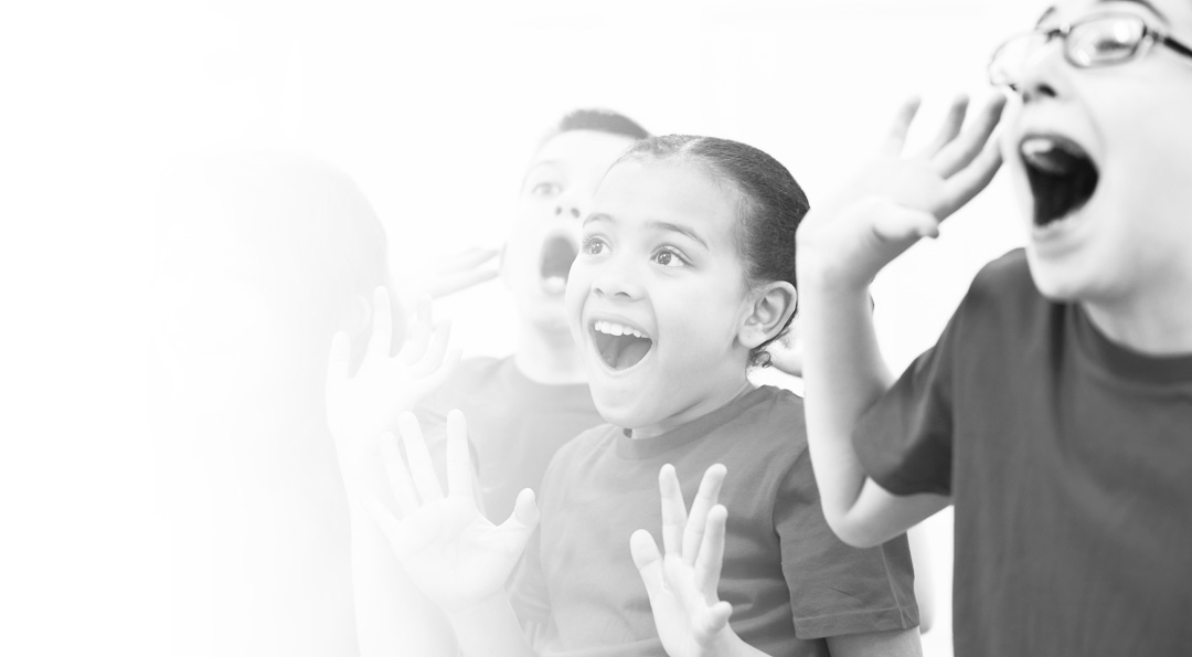 Three children expressing surprise or excitement with open mouths and raised hands.