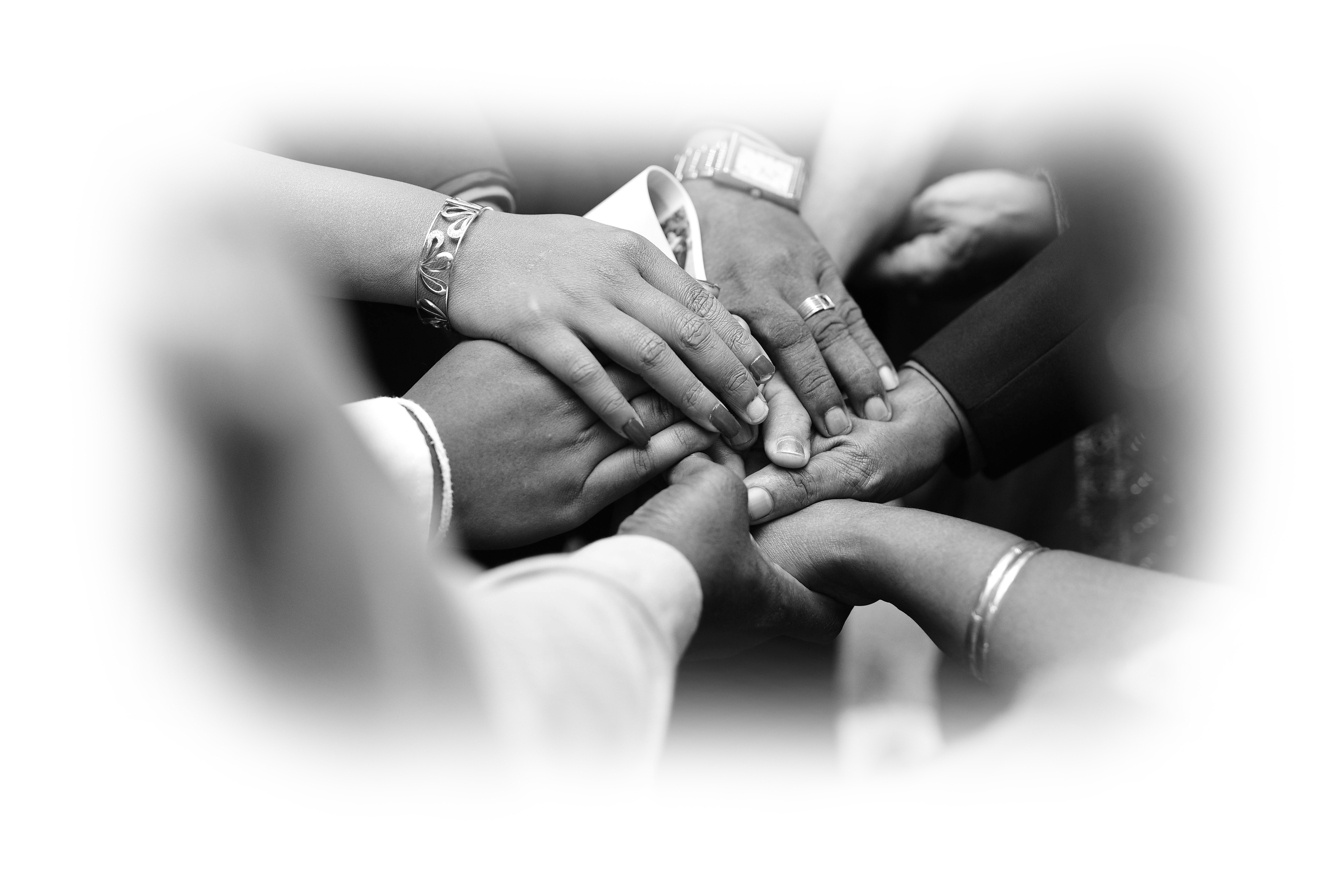 Black and white image of multiple hands stacked together in a gesture of unity and support.