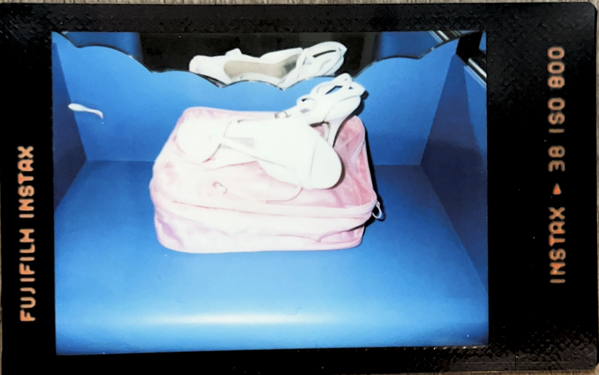 A photo taken with a flash on an instant film camera. The flash has caused it to be overexposed. The photo features white shoes atop their pink case and a blue shelf.