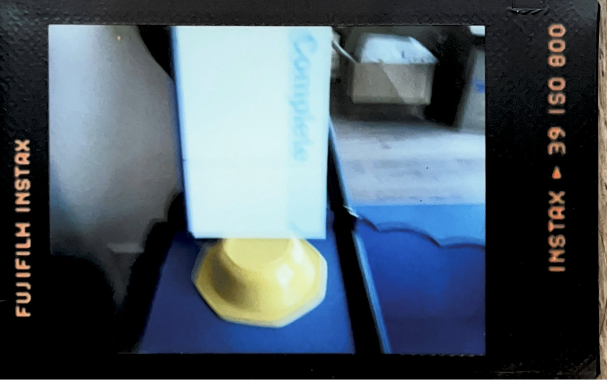 A photo taken with a flash on an instant film camera. The flash has caused it to be overexposed. The photo is blurry and features a white and blue journal on a yellow stand.
