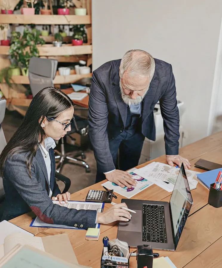 A senior partner working alongside an analyst over printed financials and a laptop.