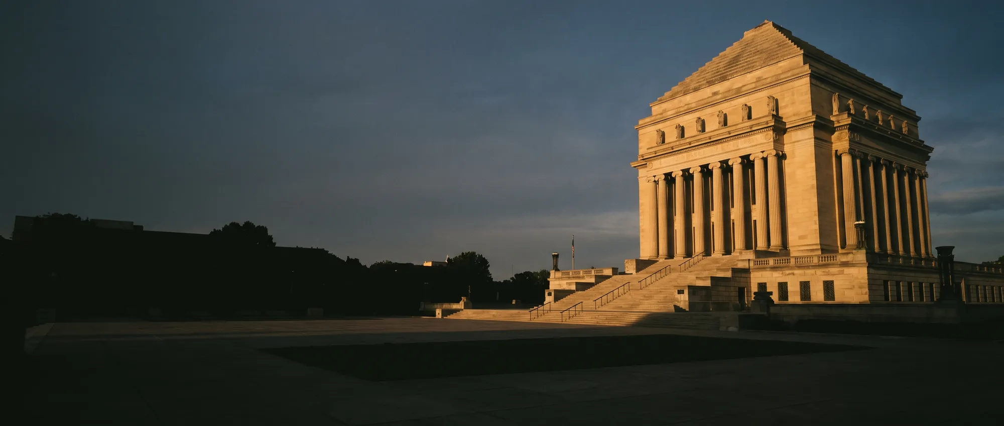 The Indiana World War Memorial in Indianapolis at dusk, its Indiana limestone colonnade lit gold above the plaza steps