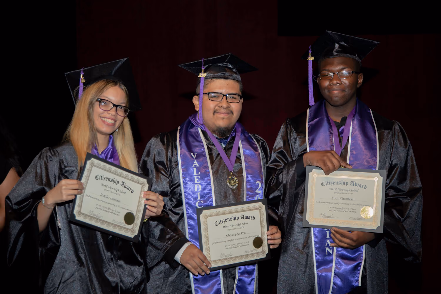 Three graduates holding Citizenship Award certificates at commencement ceremony