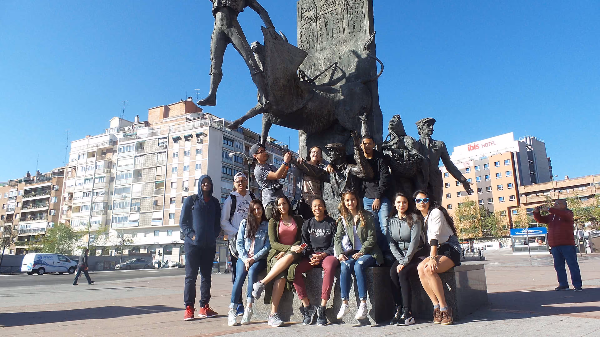 Students posing together at a bronze monument in a city square