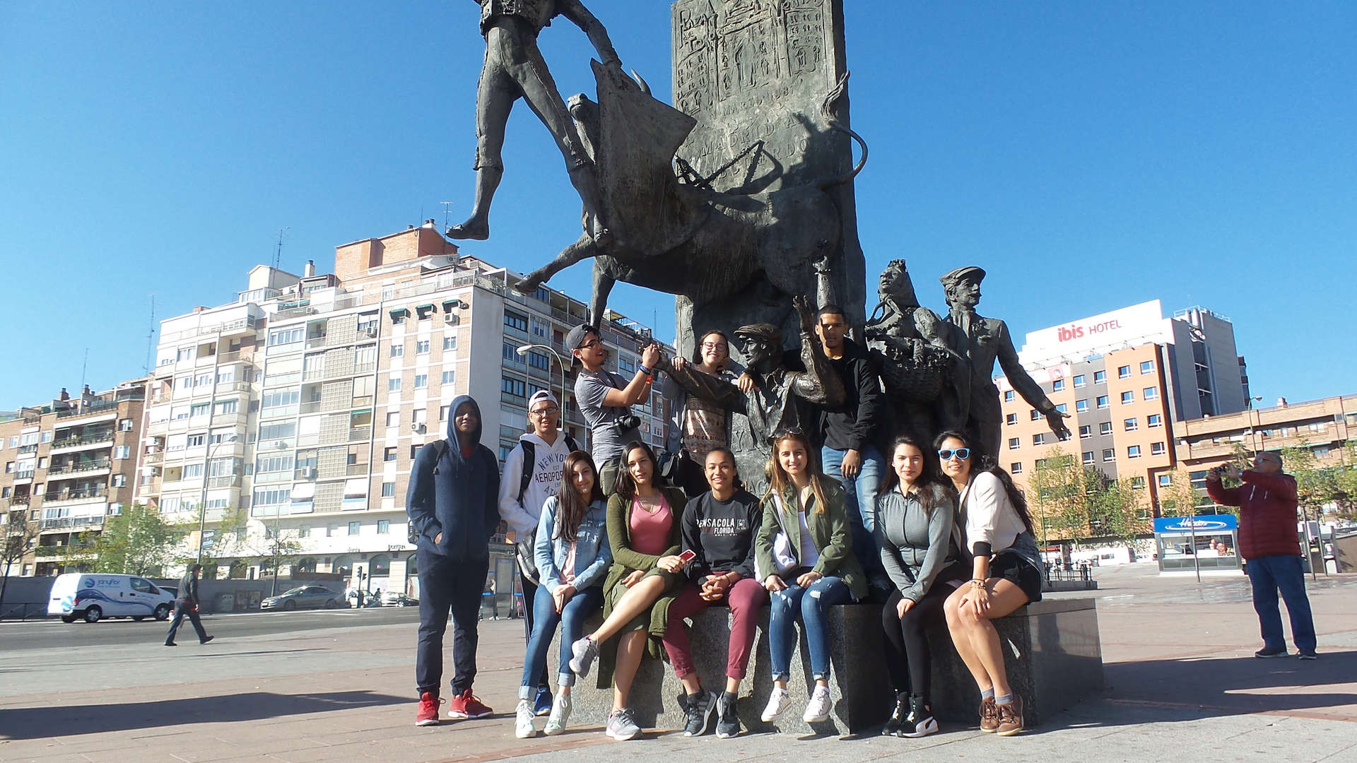 Students posing together at a bronze monument in a city square
