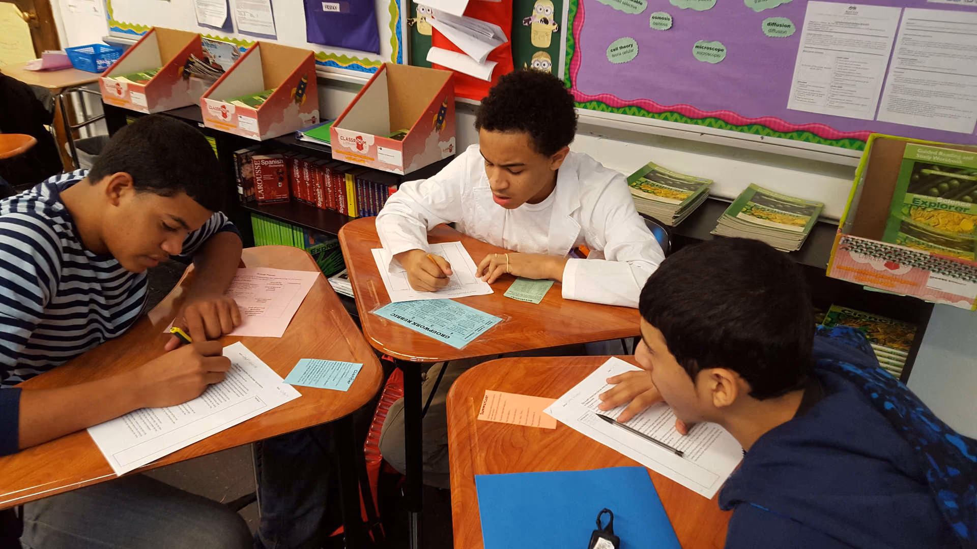 Three middle school students working on worksheets at classroom desks