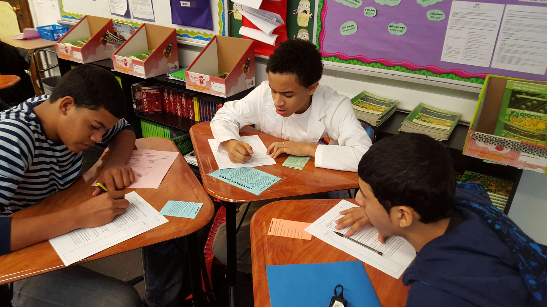 Three middle school students working on worksheets at classroom desks