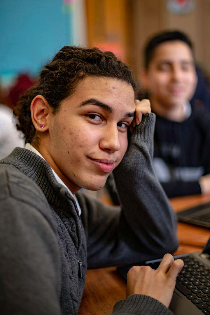 Student smiling at camera with laptop during classroom lesson