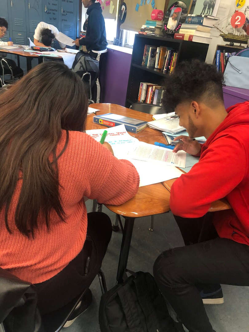 Two high school students collaborating on written work at classroom desks