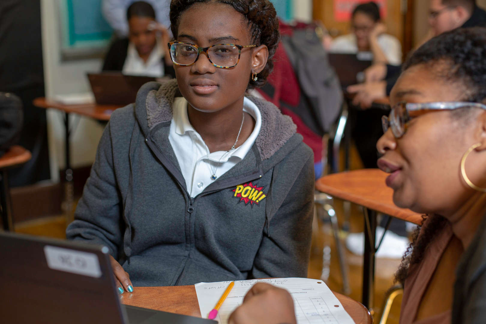 Student and teacher discuss work together in a busy classroom