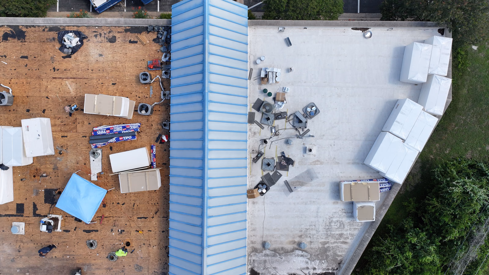 Aerial view of a large commercial building mid-reroof with membrane material staged and a worker present.