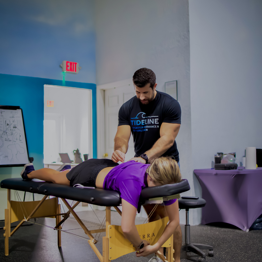 Therapist in a Tideline shirt working on a woman lying face down on a treatment table.