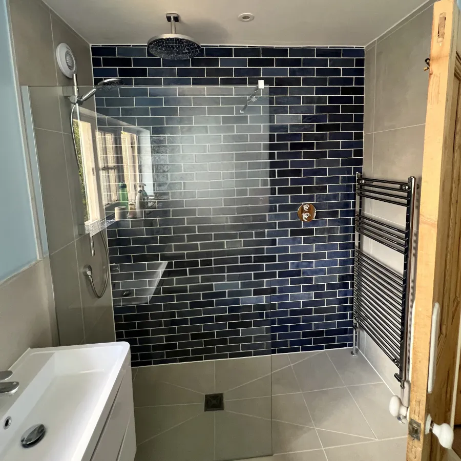Modern bathroom with walk-in shower, dark blue subway tile wall, glass partition, and white vanity sink.
