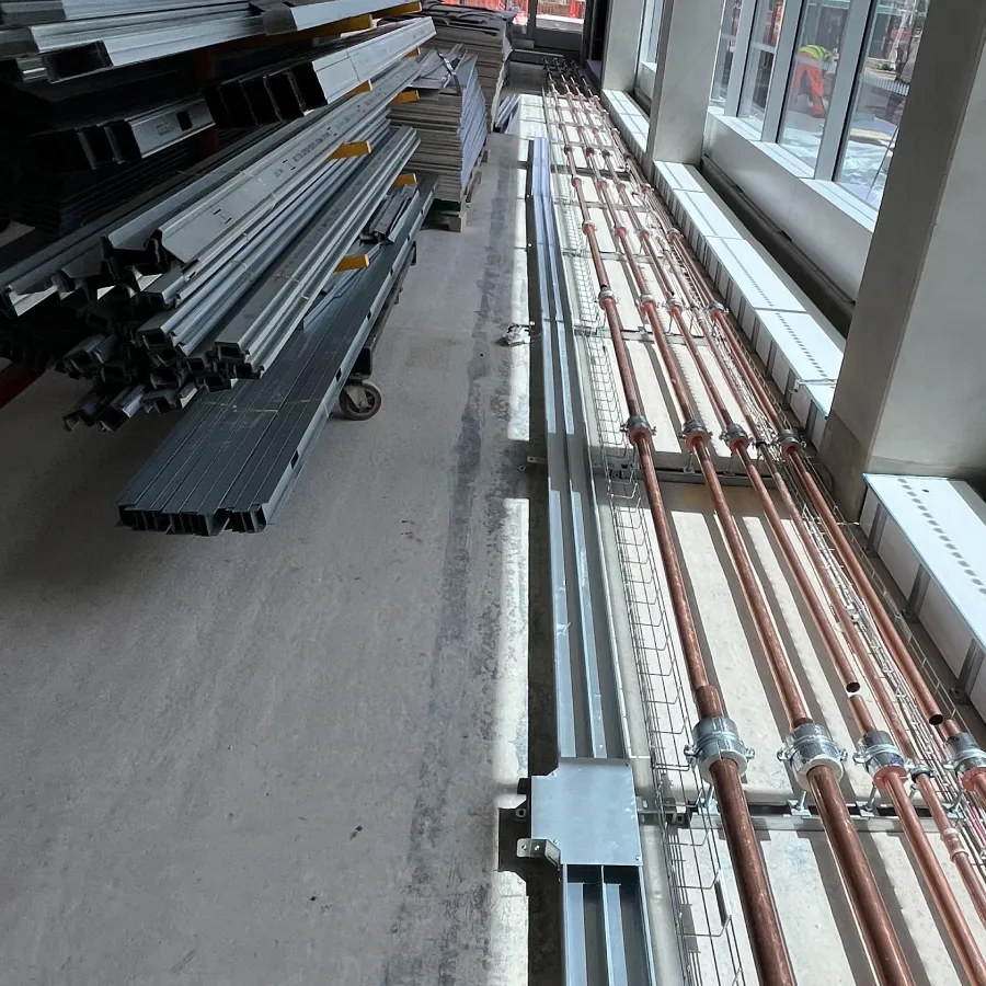 Copper pipes installed along floor next to stacked metal construction materials in a building under construction.