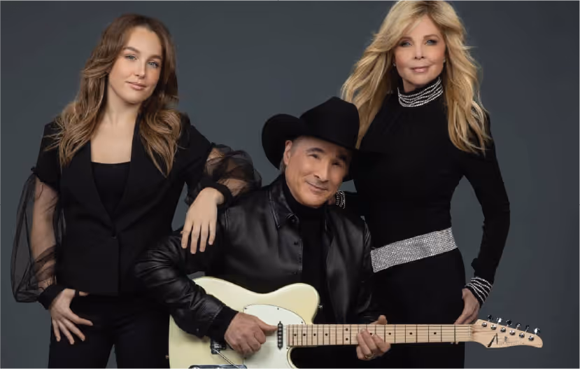 Clint Black holding an electric guitar, standing between his wife Lisa Hartman Black and their daughter Lily Pearl Black.