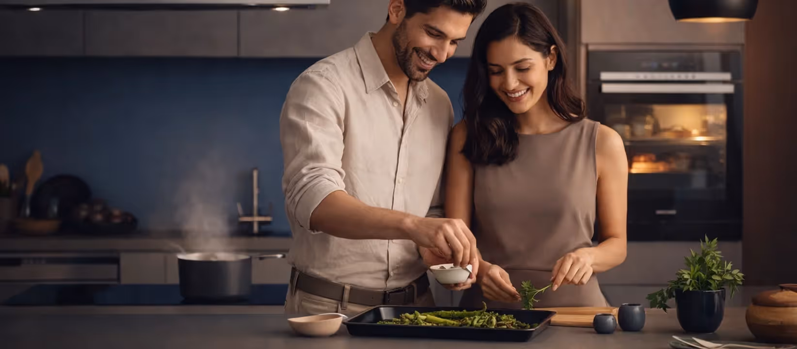 Smiling couple adding herbs to asparagus on baking tray in modern kitchen.