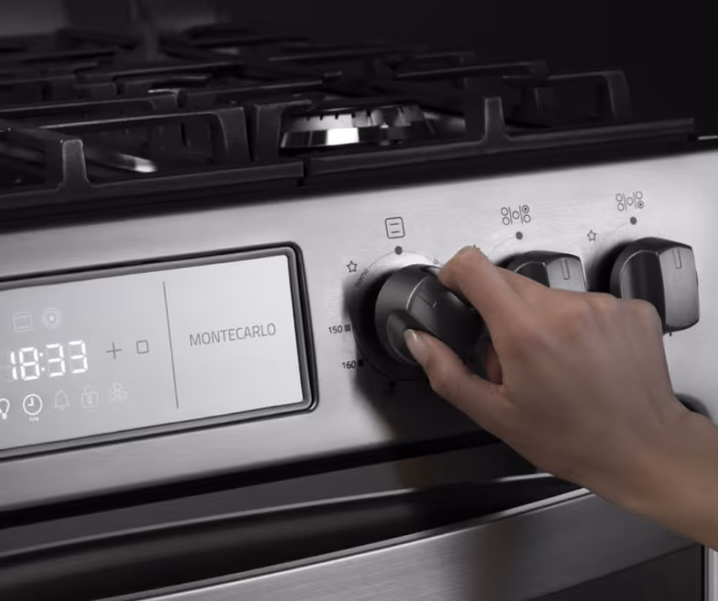 Hand turning a knob on a stainless steel Montecarlo gas stove with digital display showing 18:33.