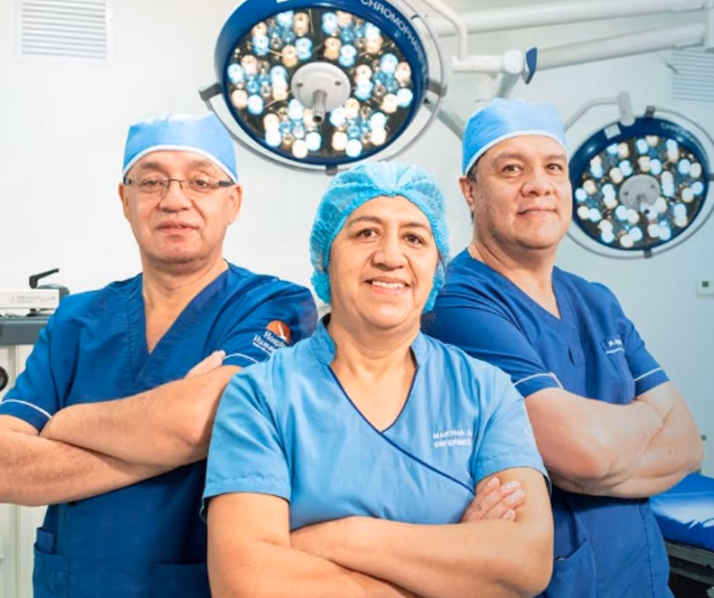 Three medical professionals in blue scrubs and caps standing with arms crossed in an operating room.