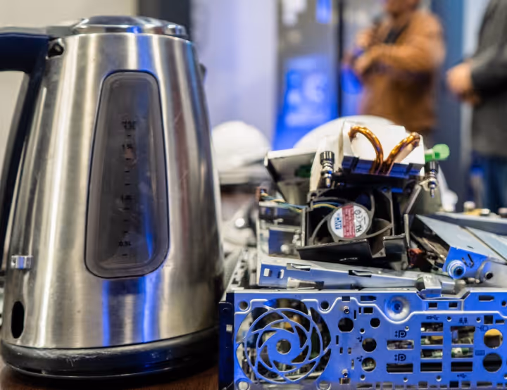 Metal electric kettle next to an open computer case with visible cooling fans and copper heat pipes.