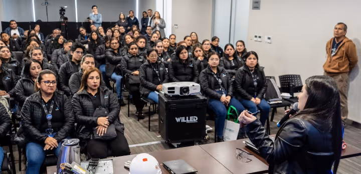 Woman speaks to attentive audience seated in rows in a modern conference room.