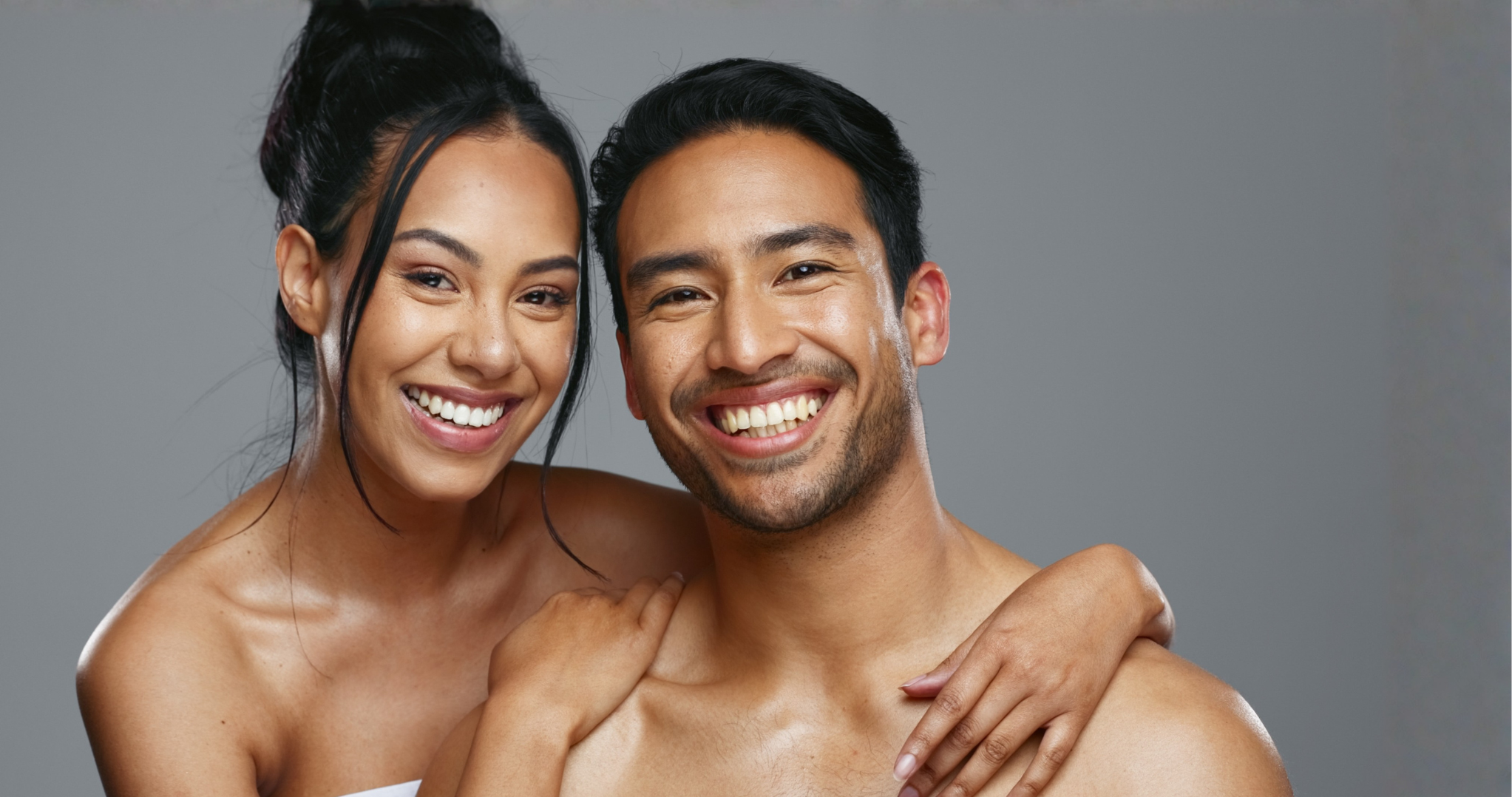 Smiling couple embracing outdoors near water with modern buildings in background.
