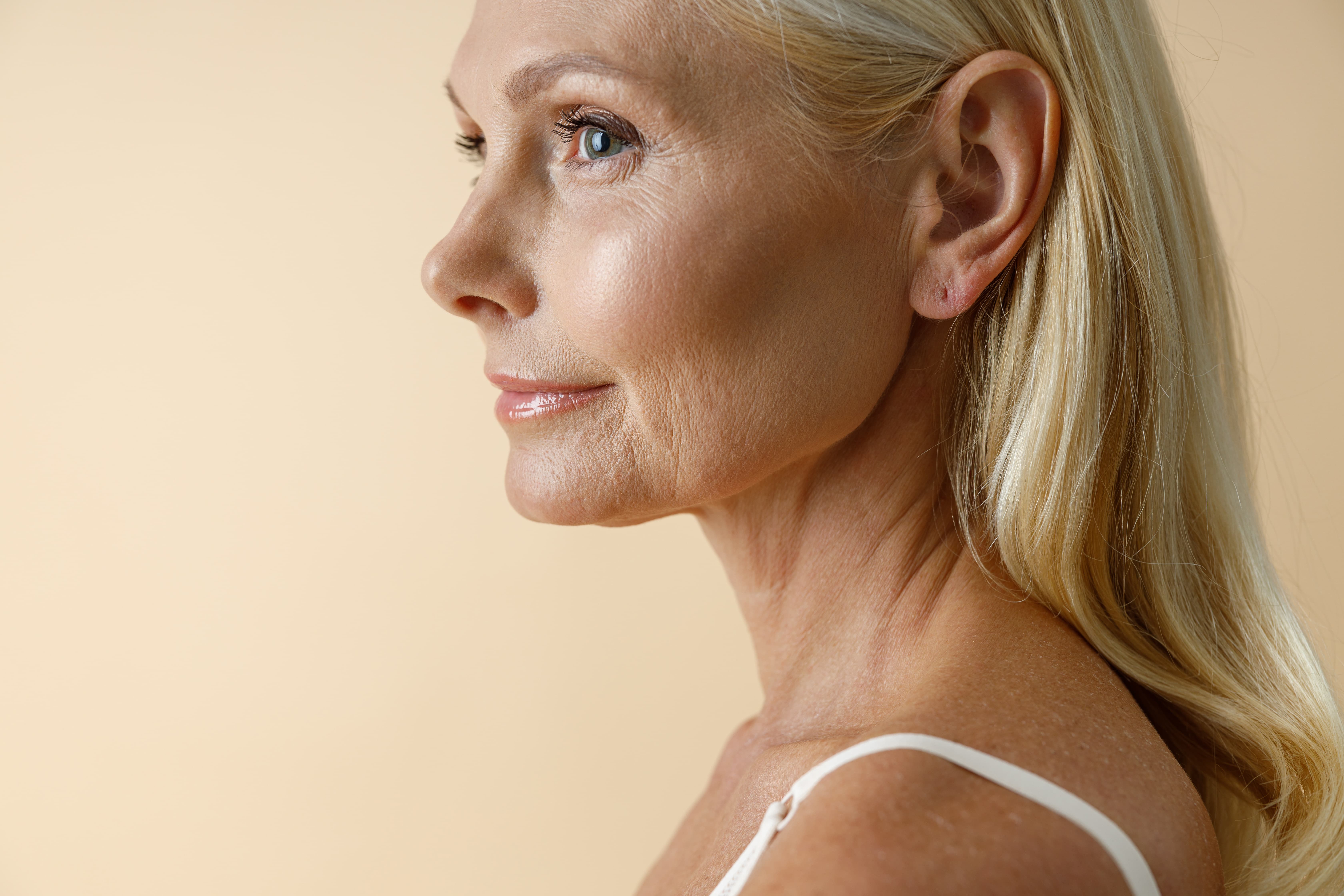 Profile of a mature woman with blonde hair and smooth skin against a beige background.