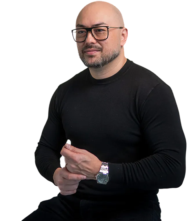 Paul Quinn with glasses wearing a black long-sleeve shirt and silver watch, sitting with hands clasped.