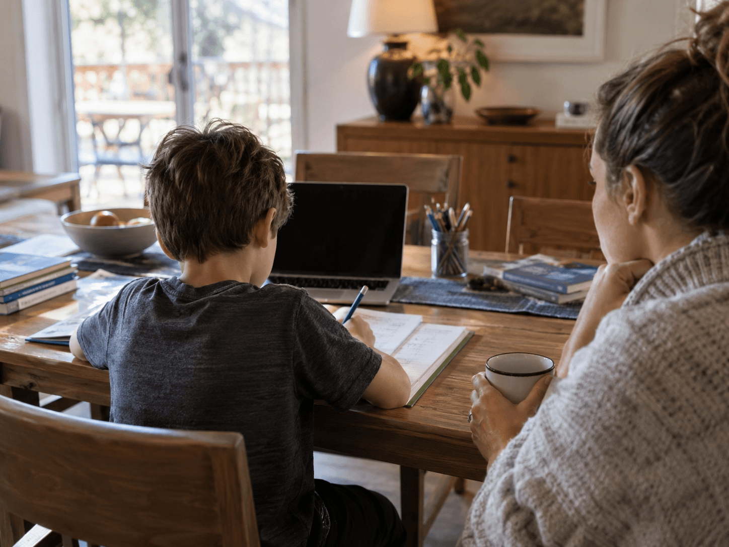 A child doing homework at a dining table while a parent sits beside him.