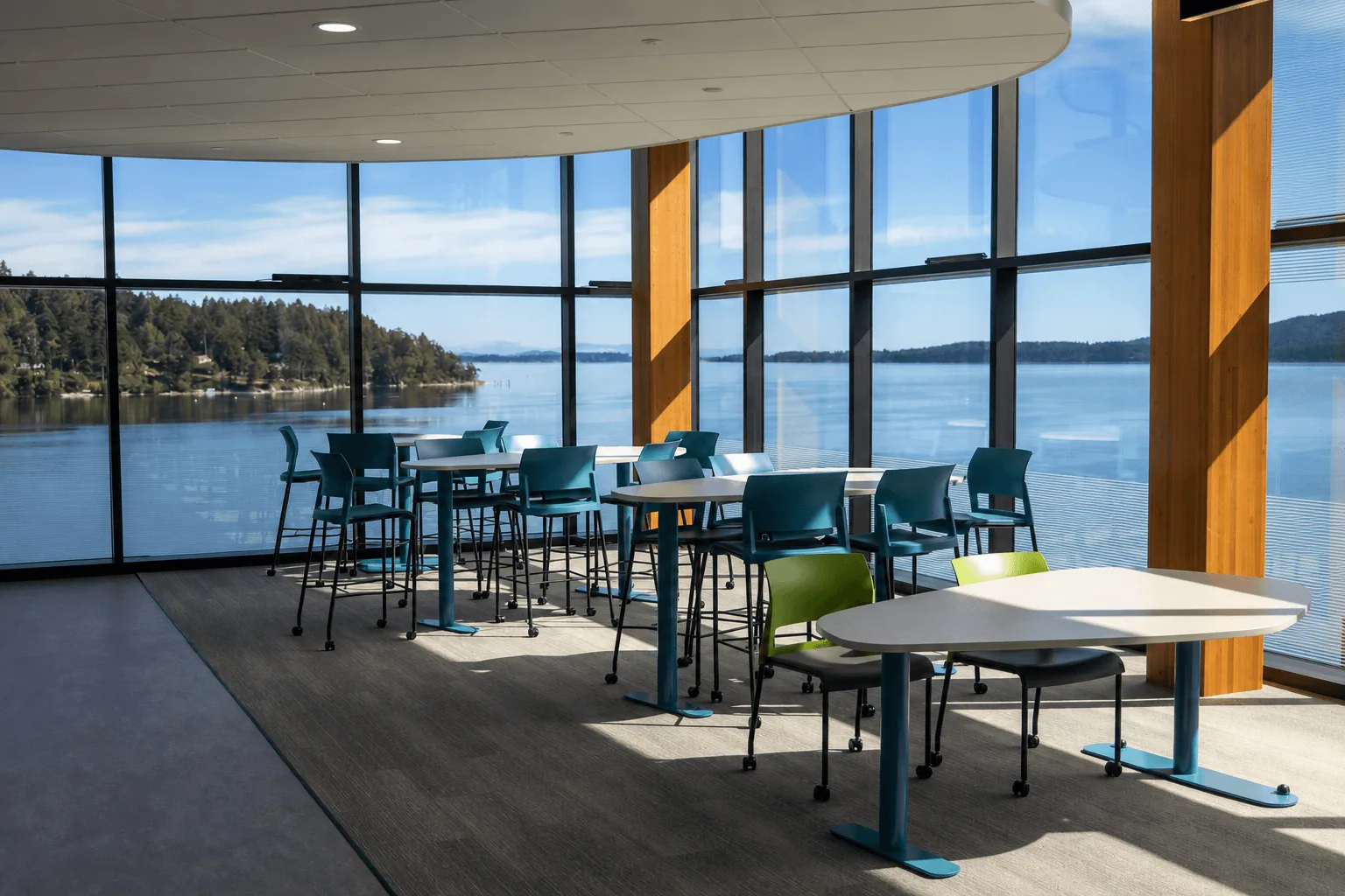 Tables and chairs in a curved room with floor-to-ceiling windows overlooking the water.