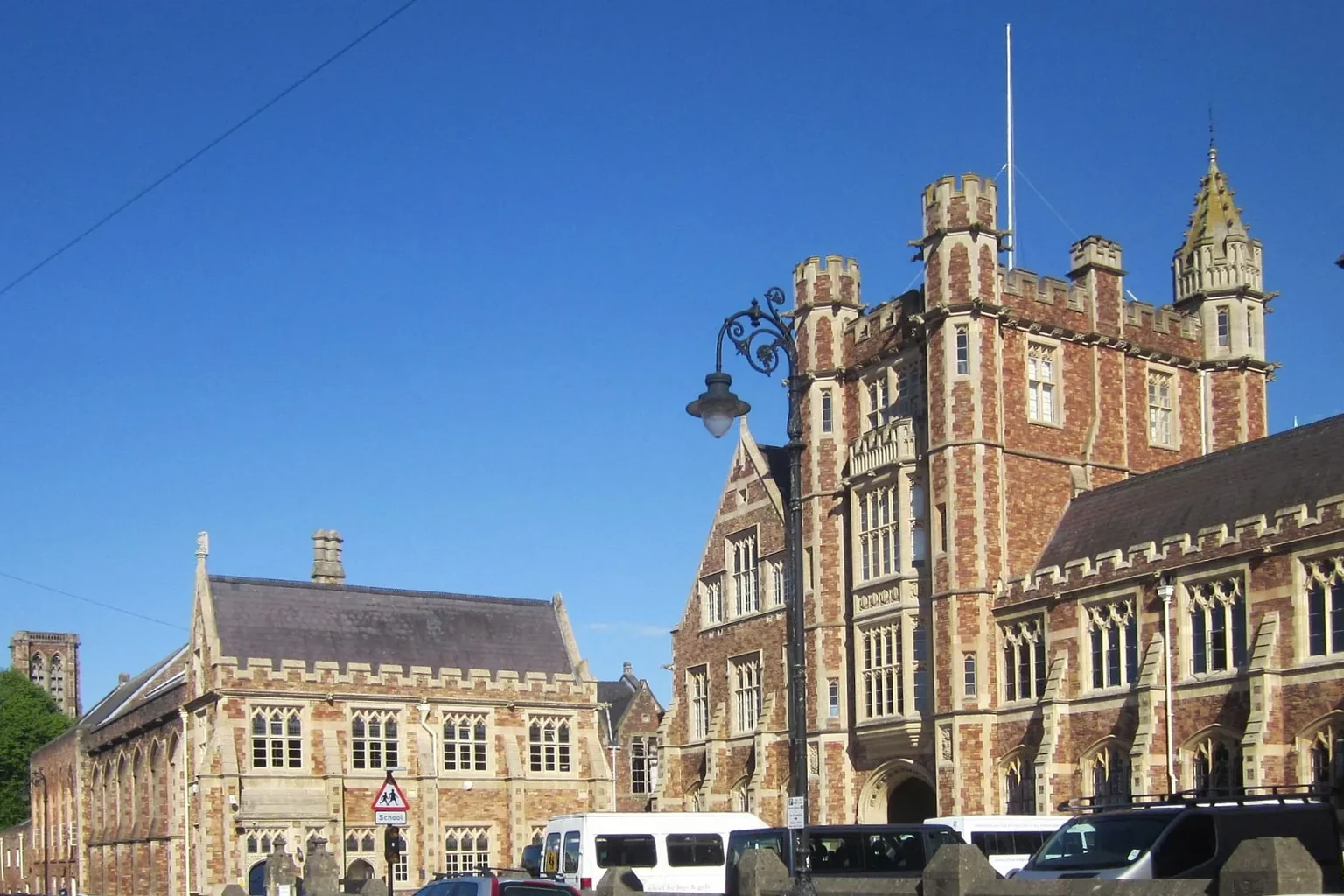 The red-brick buildings and towers of Clifton College along College Road under a blue sky.