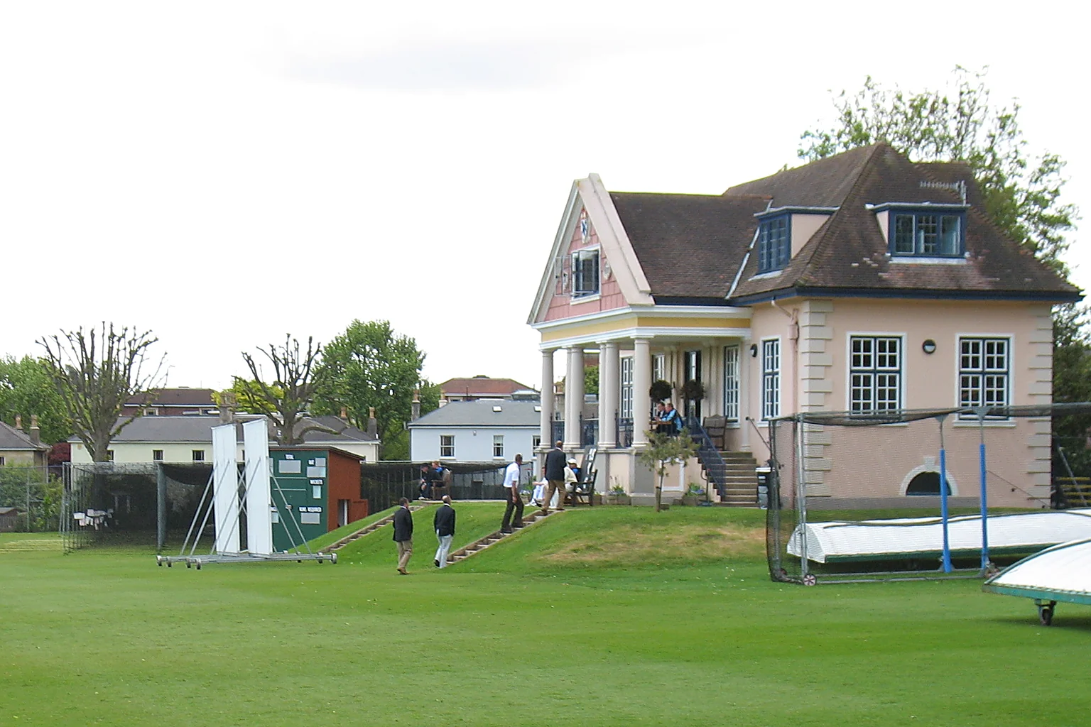 The cricket pavilion at Clifton College, a pale house with a columned porch at the edge of a playing field.