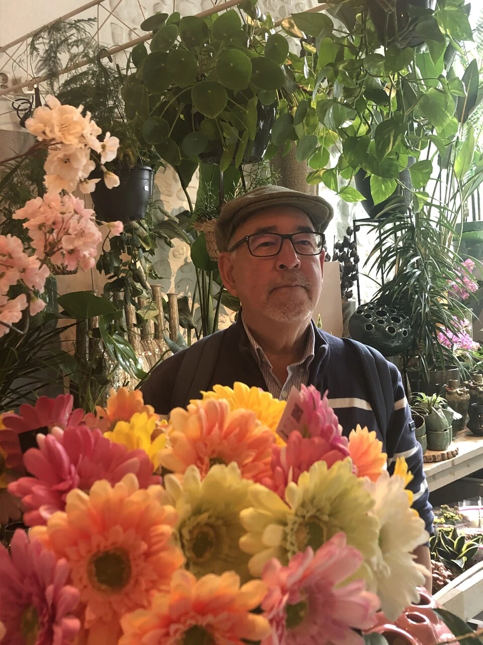 Marcel de Lannoy today, in a flat cap and glasses, behind a bouquet of gerberas