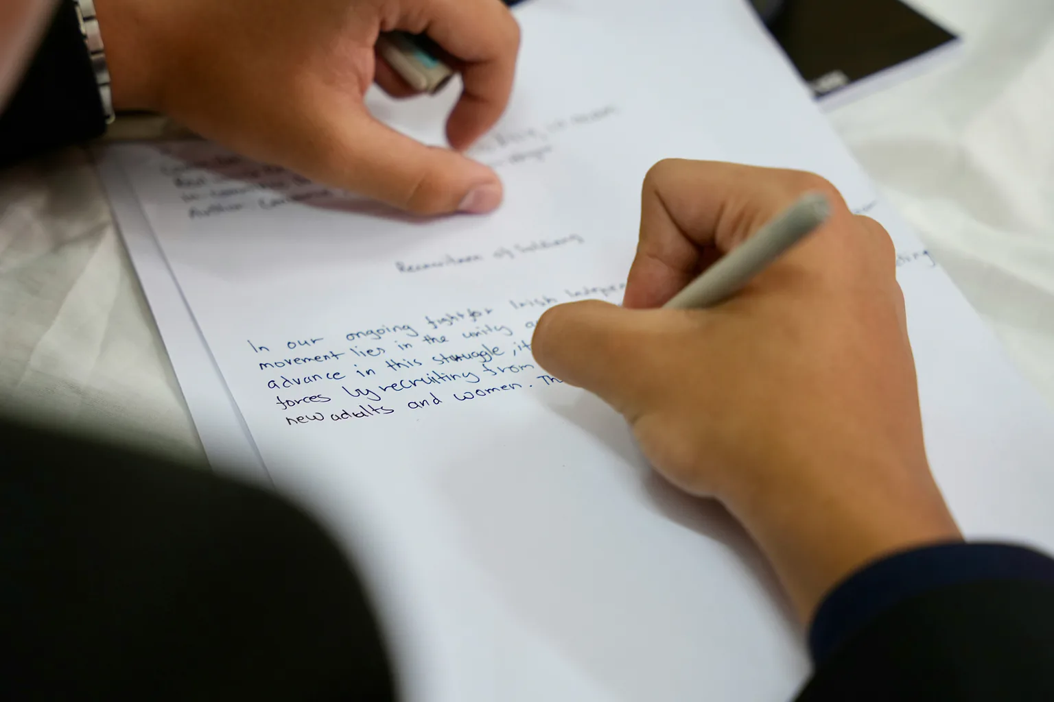 A hand writing an essay answer on a sheet of paper