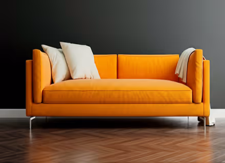 Oranje bank met witte kussens en een deken tegen een donkere muur op een houten vloer.