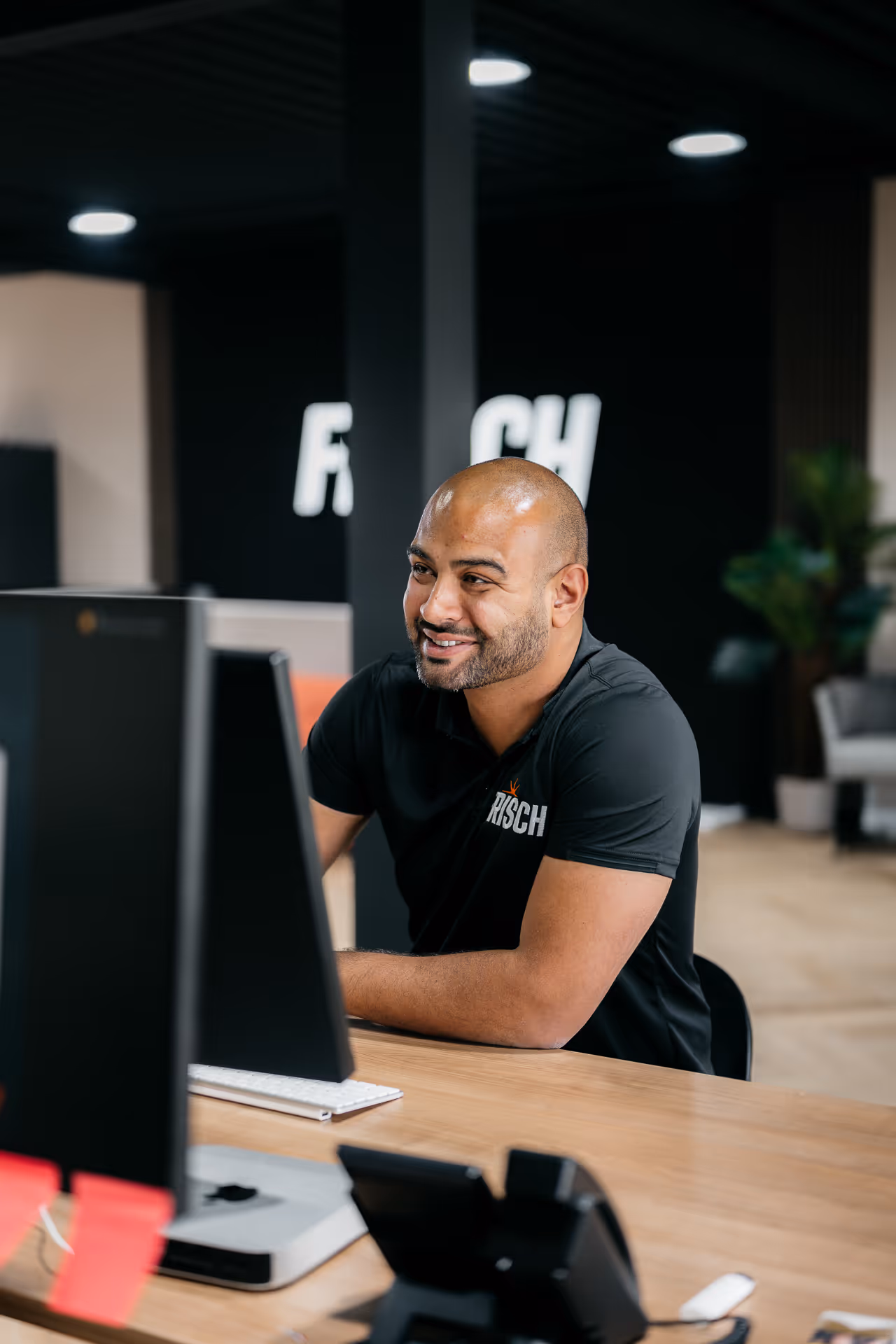 Man zit glimlachend achter bureau en werkt op computer in modern kantoor.