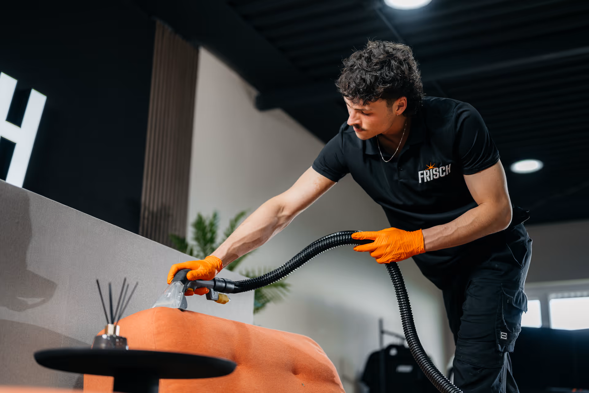 Man in oranje handschoenen die een oranje bank stofzuigt in een moderne woonkamer.