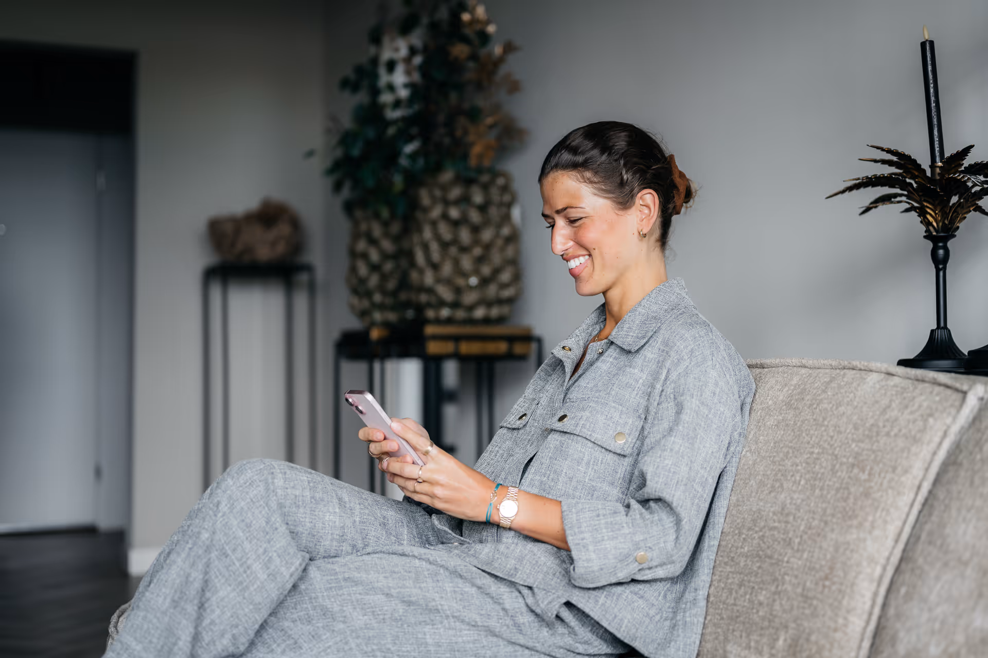Vrouw zit op bank en glimlacht terwijl ze op haar telefoon kijkt.