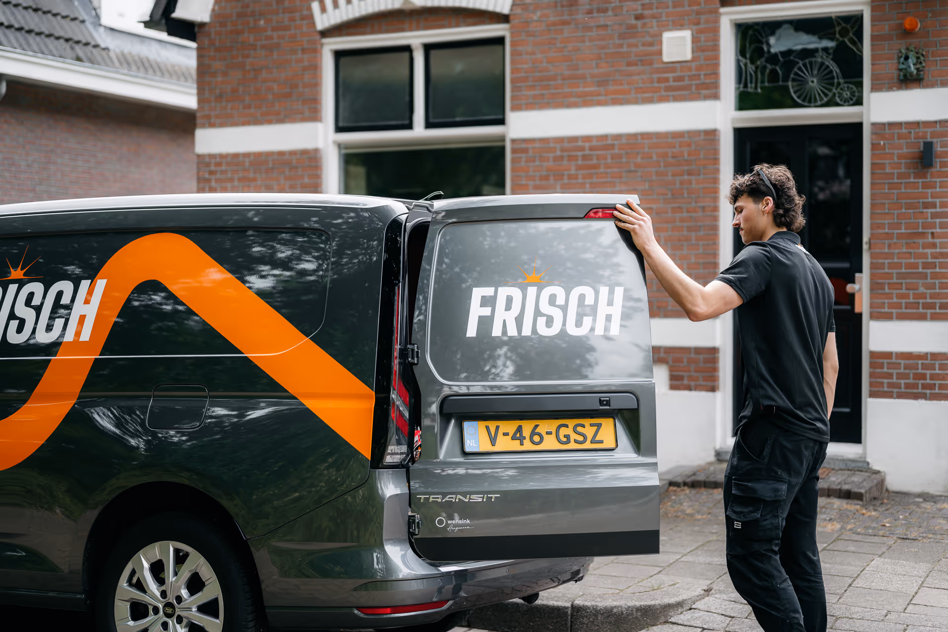 Man opent de achterdeur van een grijze bestelwagen met het logo 'FRISCH' en een Nederlands kenteken.